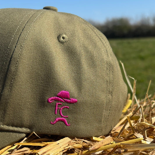 Green cap with pink logo on a background of hay and blue sky