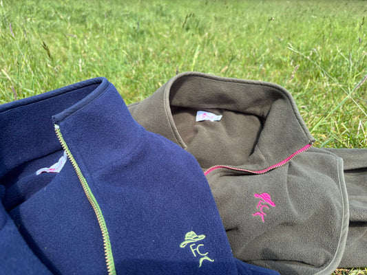 Two fleece jackets, one blue and one gray, with visible branding on a grassy background.