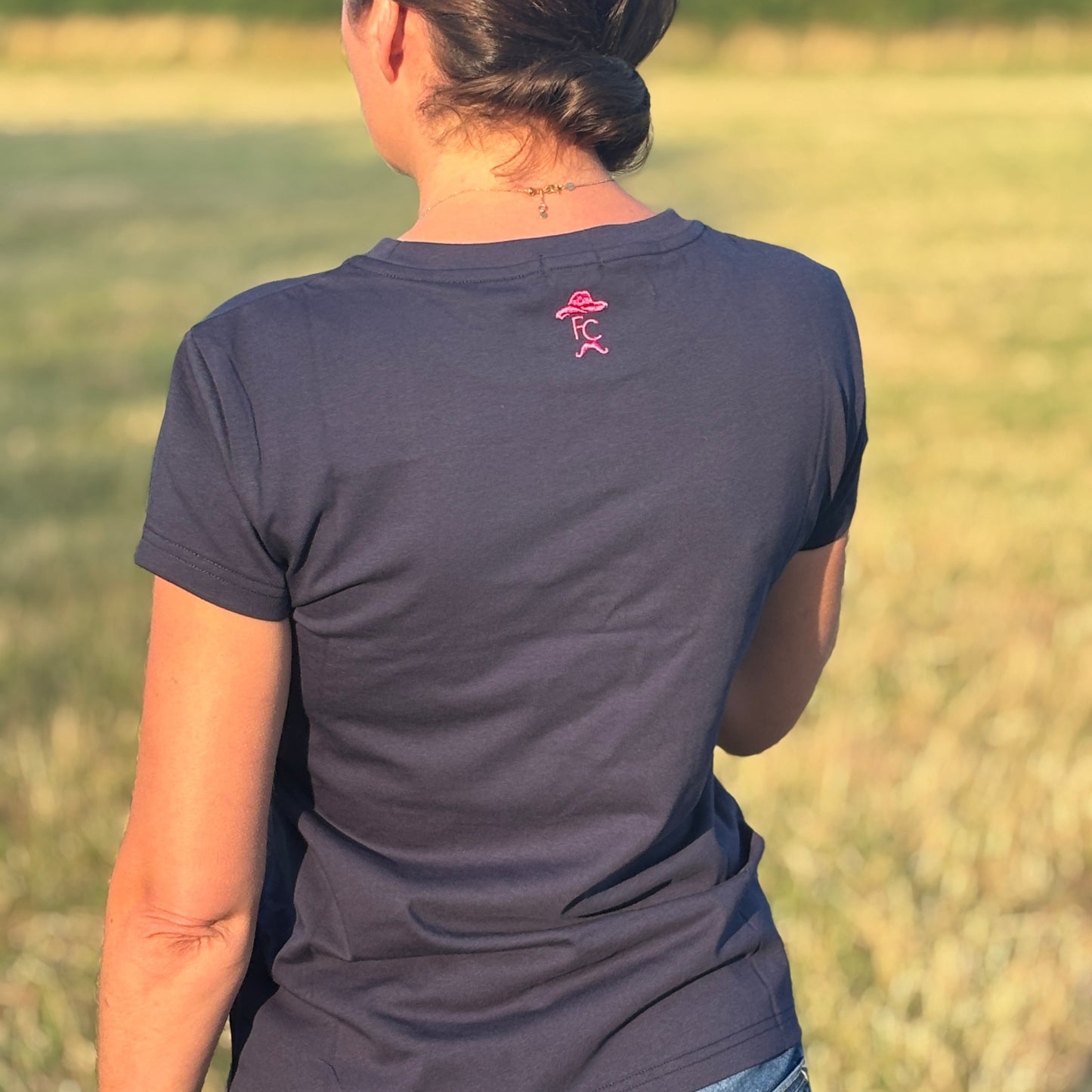 Person wearing a Fen Cowboys dark blue t-shirt with a pink logo in an outdoor setting