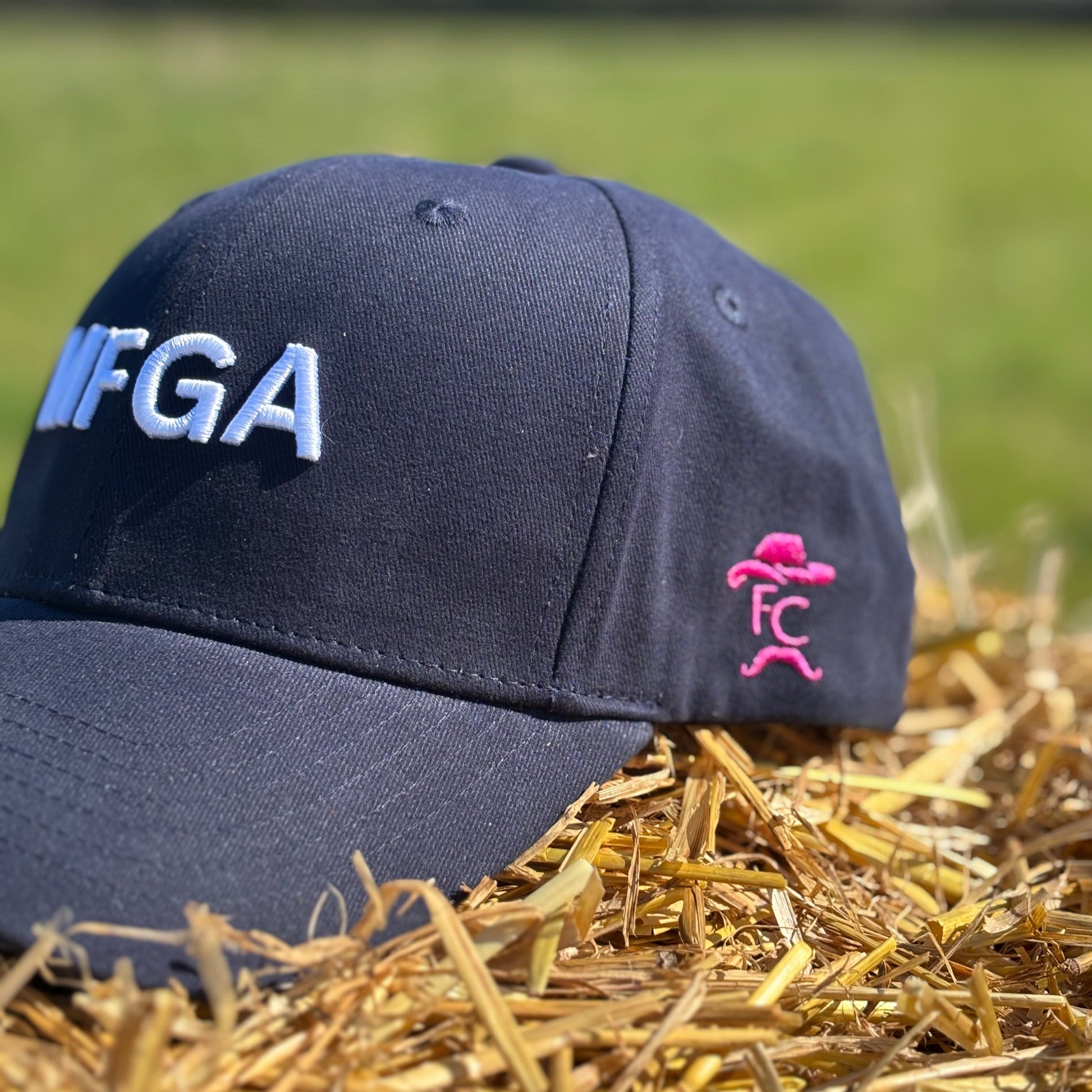 Navy blue cap with 'WFGA' logo on a stack of hay with a blurred green field background