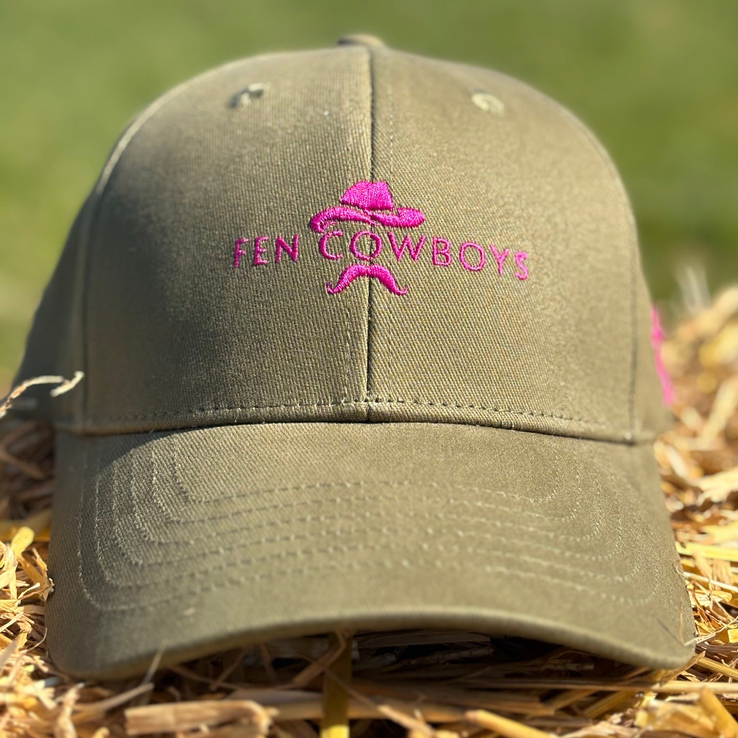Green cap with pink logo and text on a grassy background