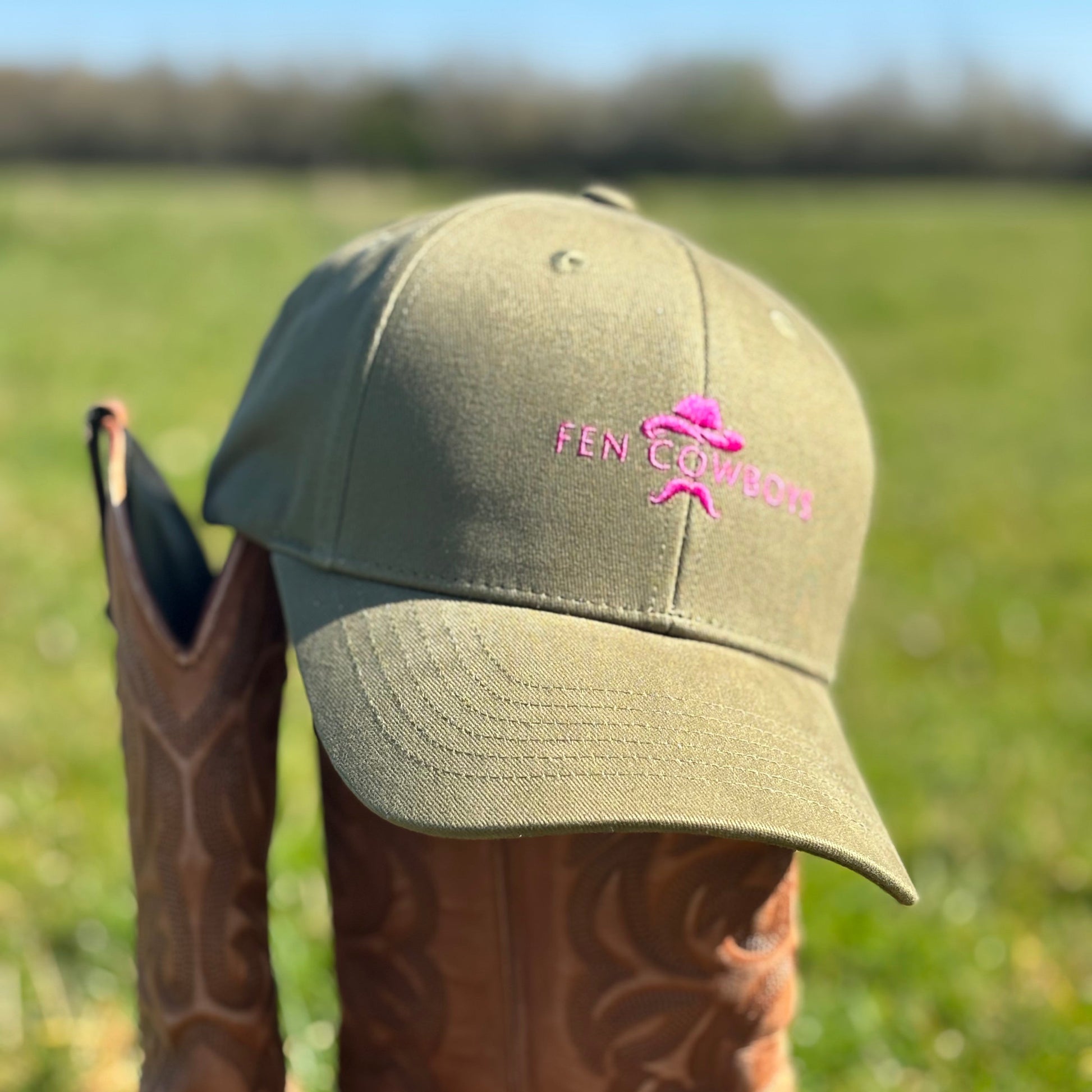 Green cap with pink logo on a brown boot in a grassy field