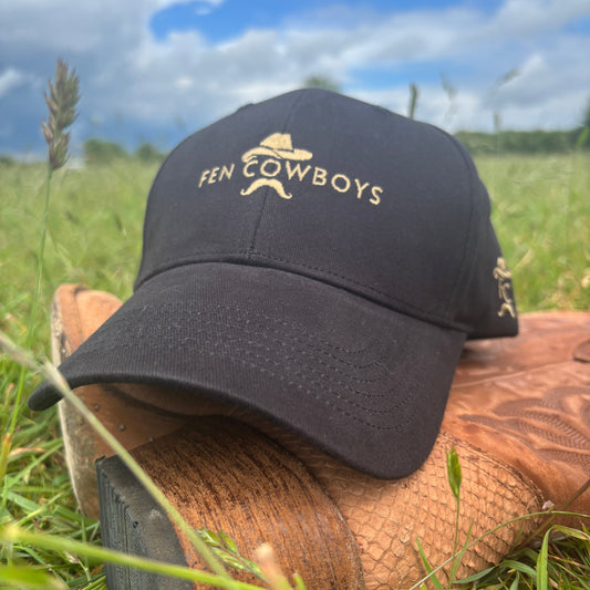 Black cap with 'Fen Cowboys' logo on a wooden duck call against a grassy background