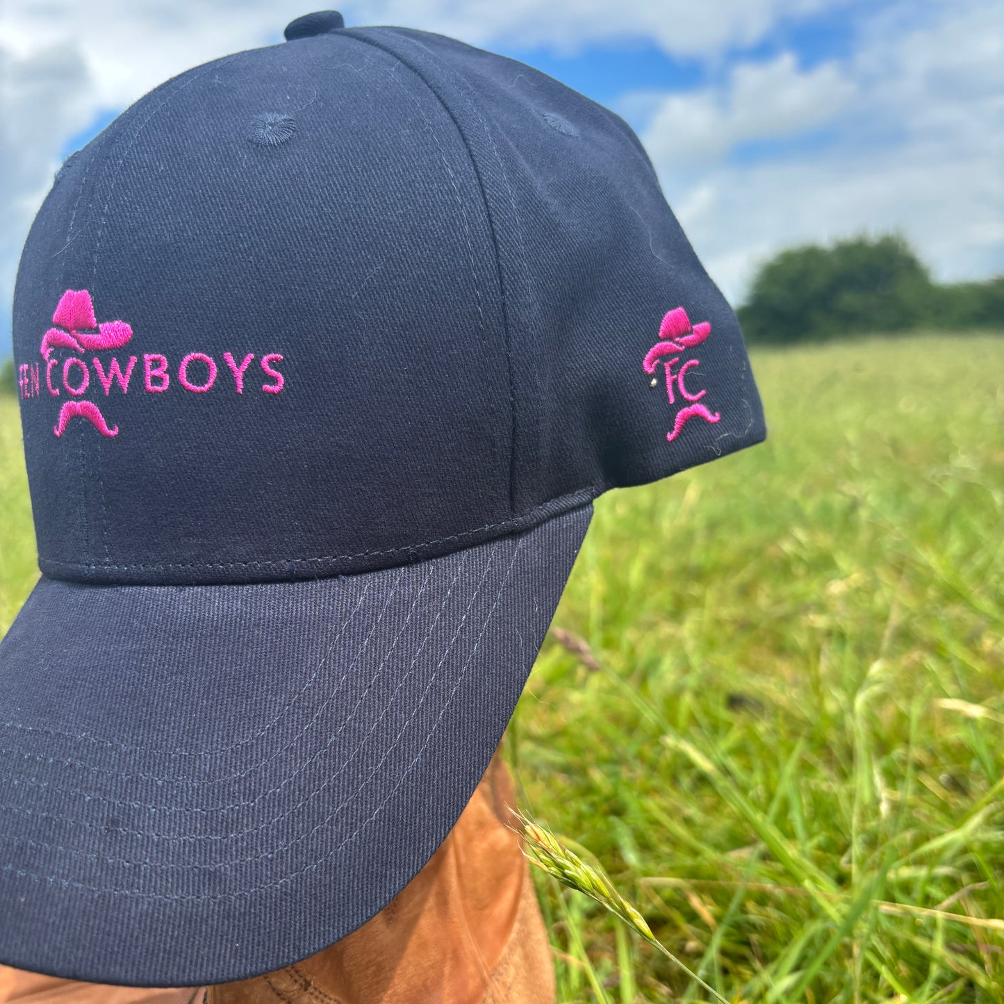 Black cap with pink logo and text on a grassy background
