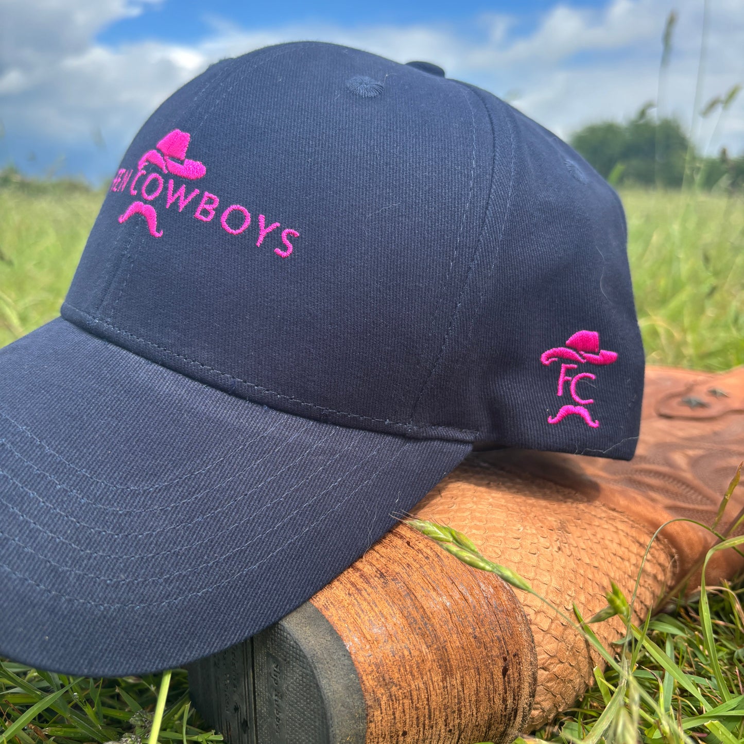 Navy blue cap with pink logo on a boot in grass near water