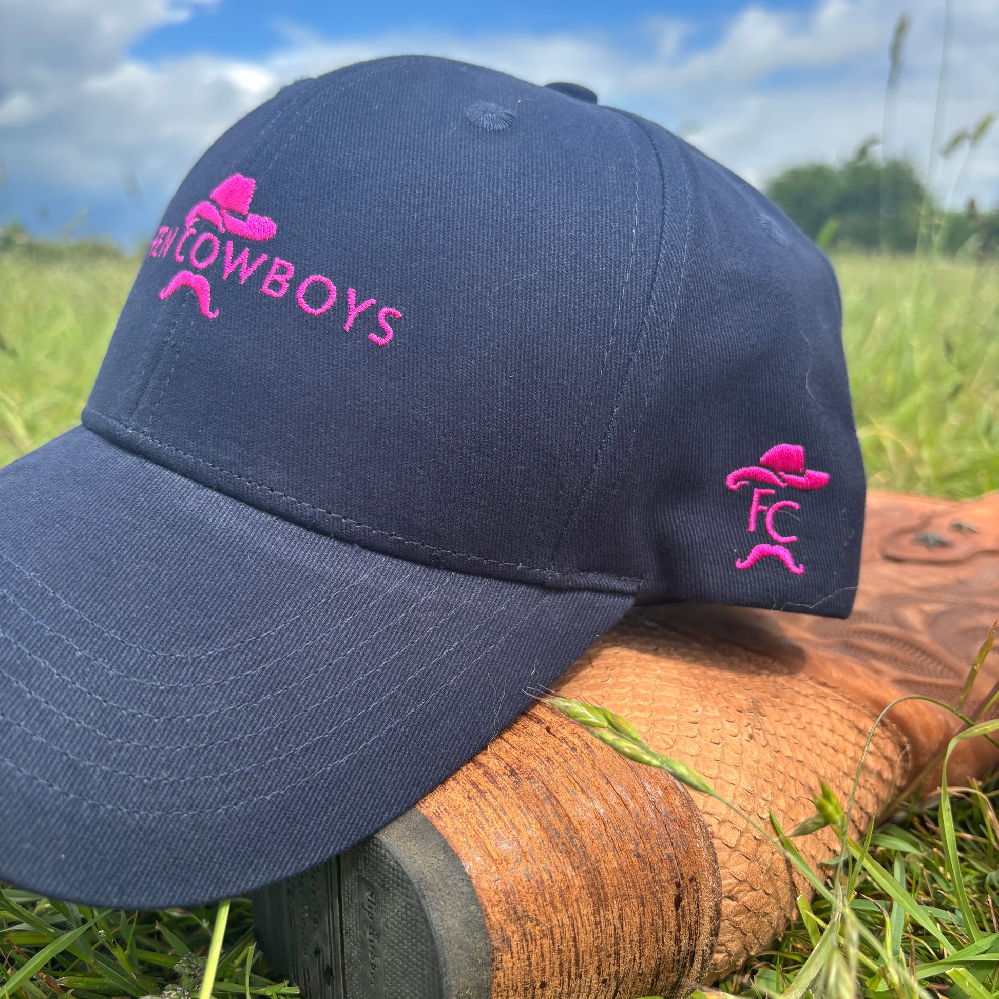 Navy blue cap with pink logo on a boot in grass near water