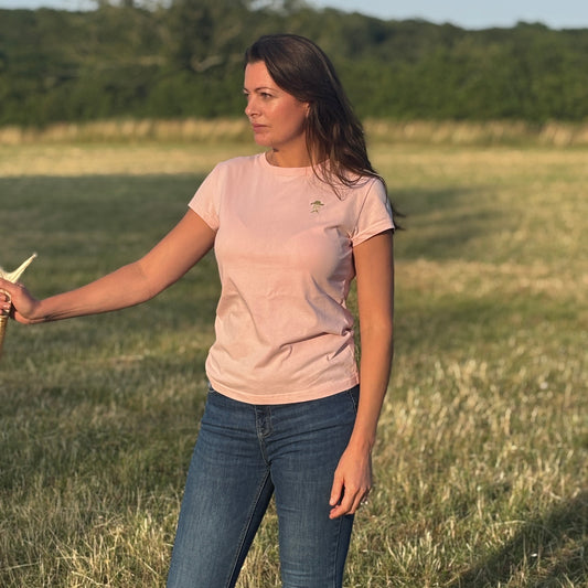 Woman standing in a field wearing a light pink t-shirt and blue jeans.