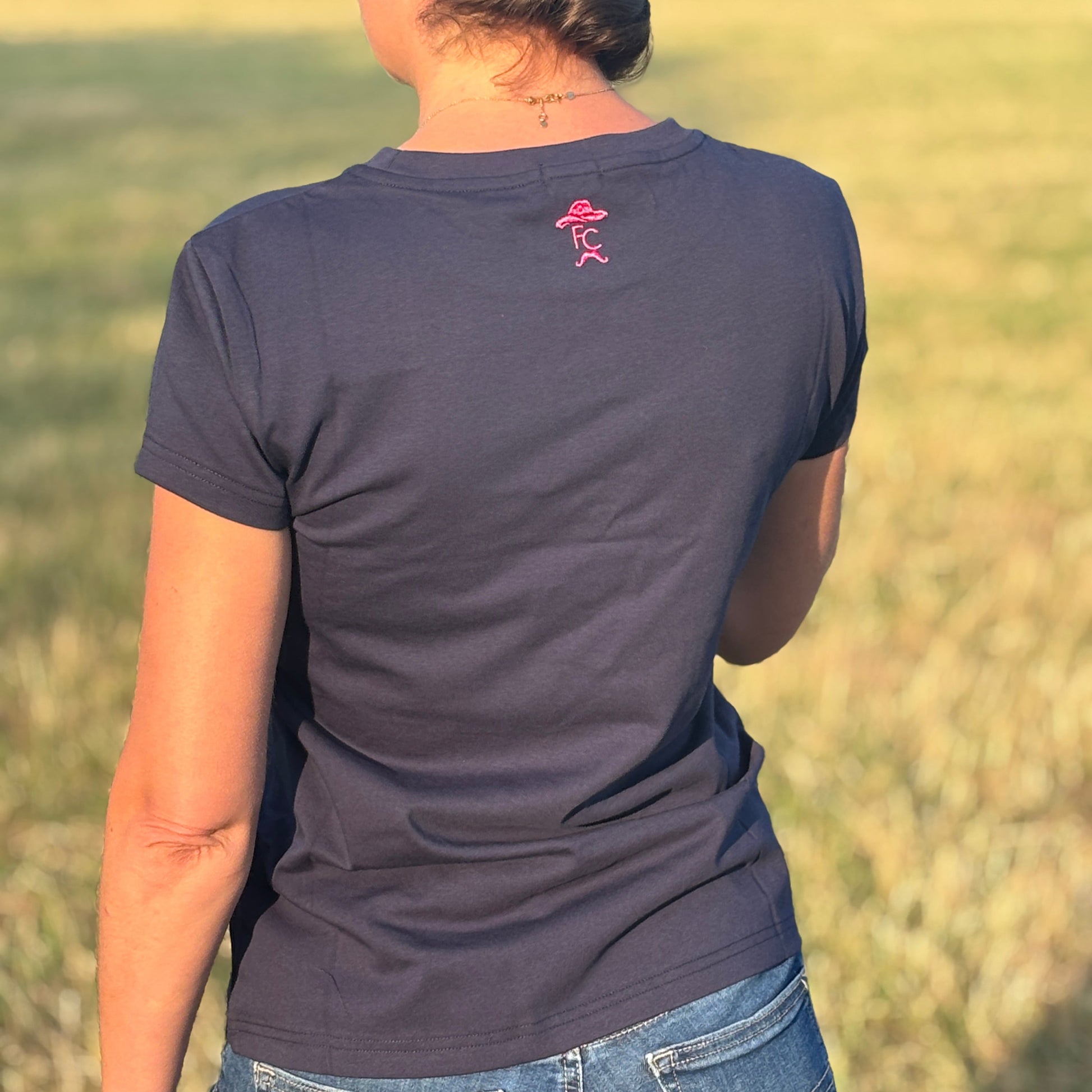 Person wearing a dark blue t-shirt with a pink logo in an outdoor setting