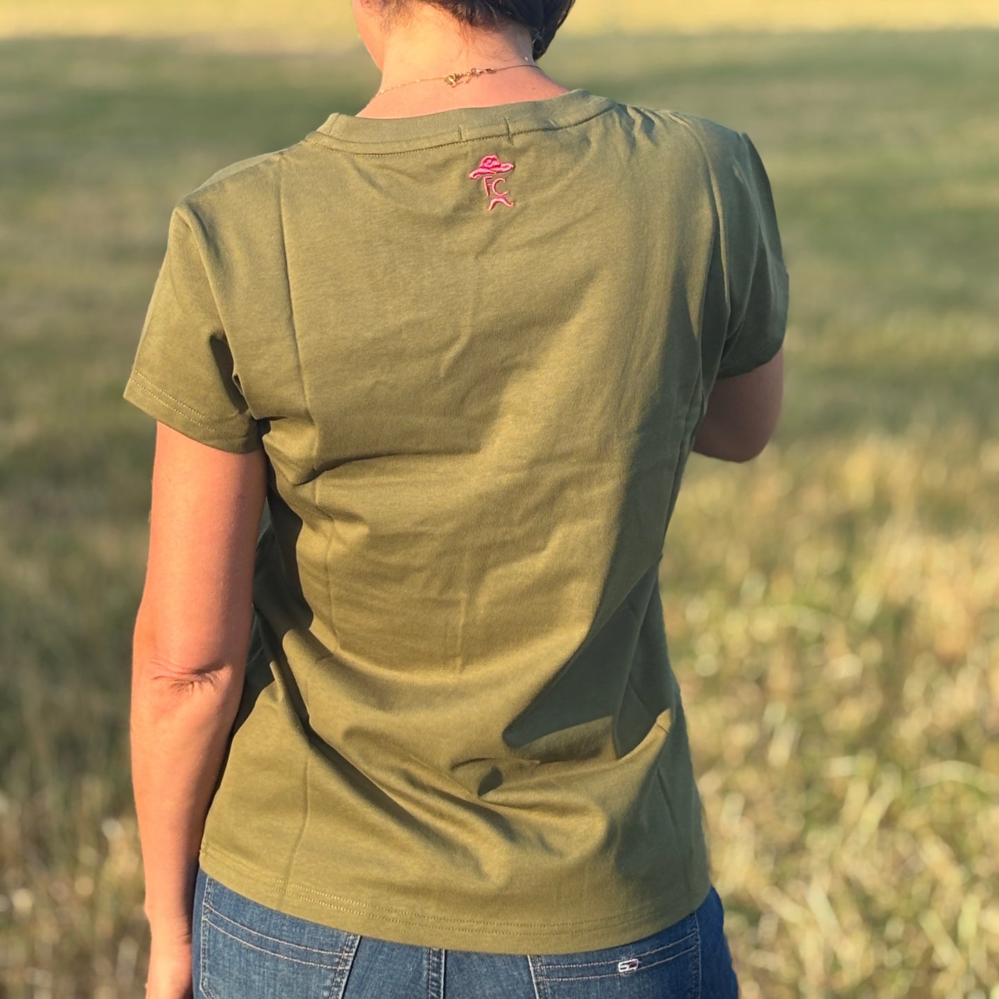 Person wearing a green shirt with a small red logo, standing in a field.