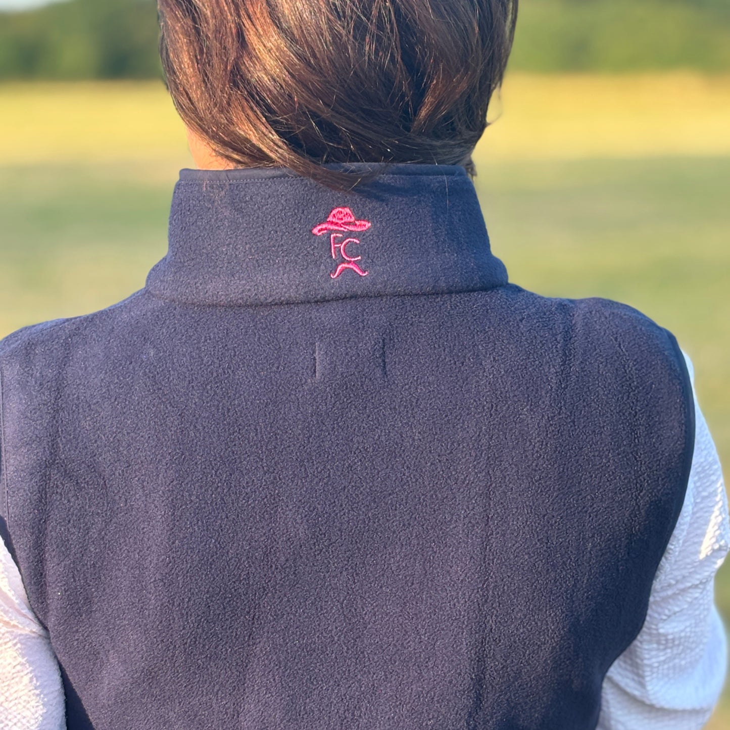 Person wearing a dark vest with a logo on the collar against a blurred natural background