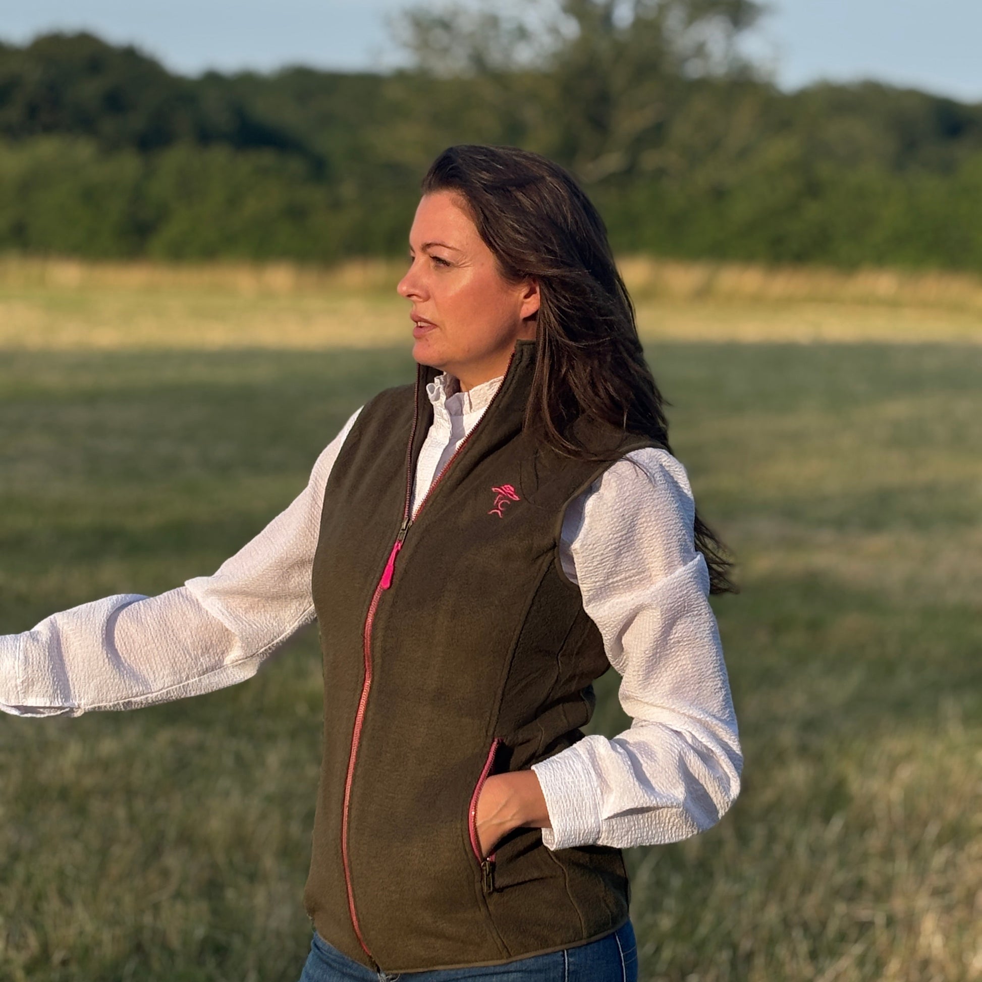 Woman wearing a brown vest with a logo in an open field