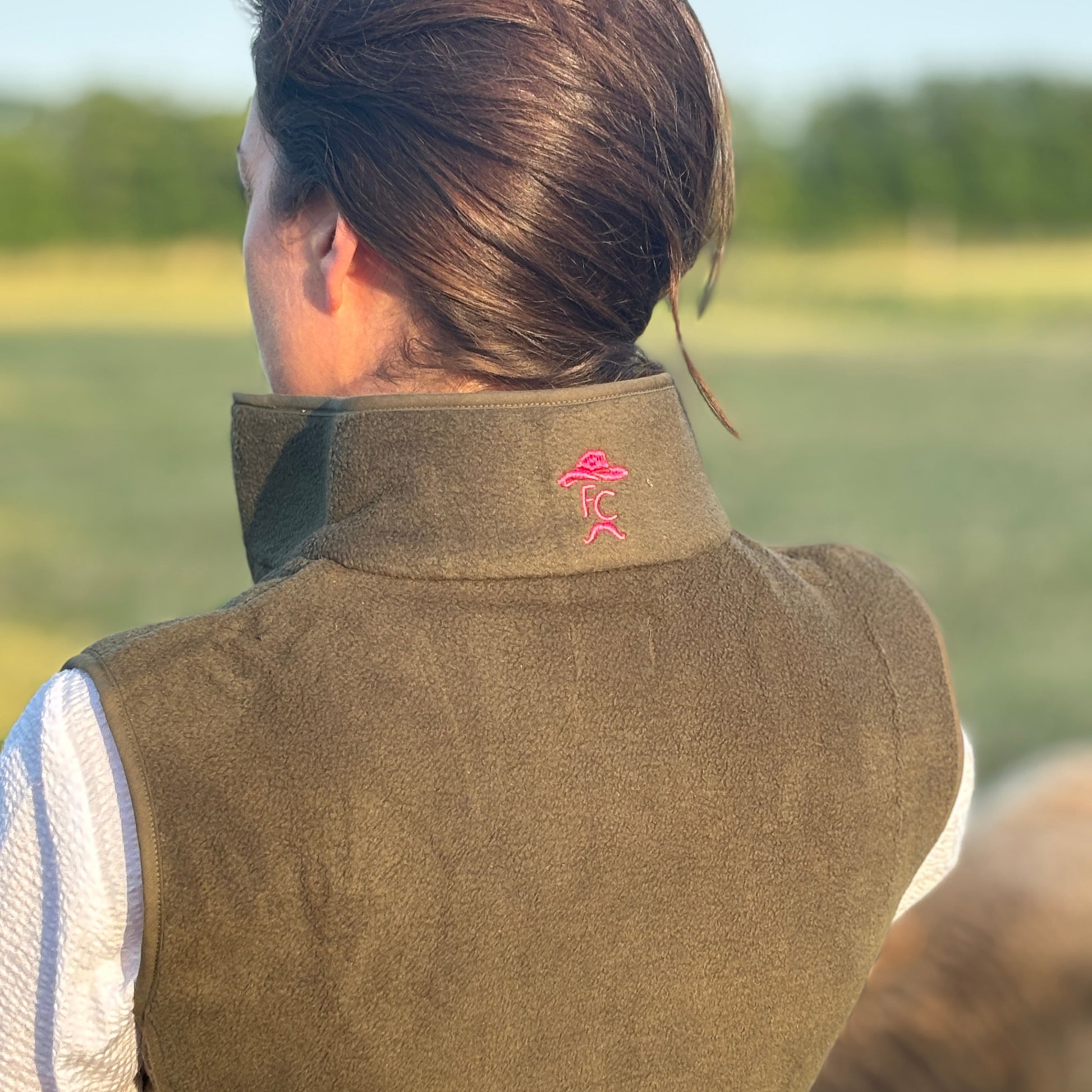 Person wearing a Fen Cowboys khaki gilet with a logo in an outdoor setting