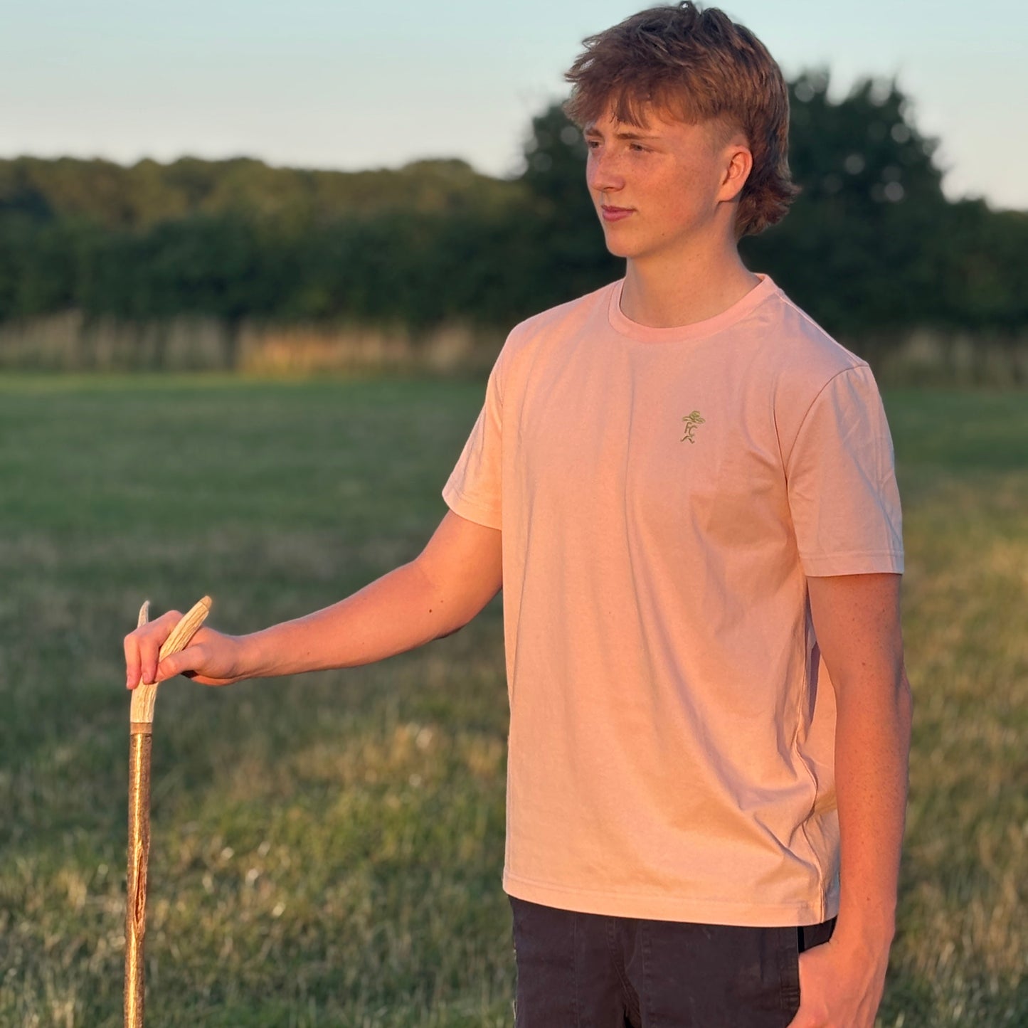 Person standing in a field holding a walking stick