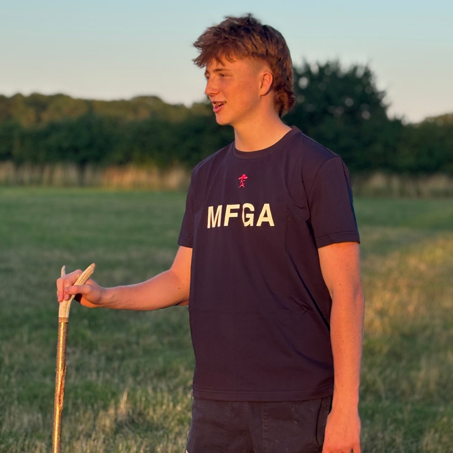 Person wearing a Fen Cowboys MFGA shirt holding a walking stick in a field