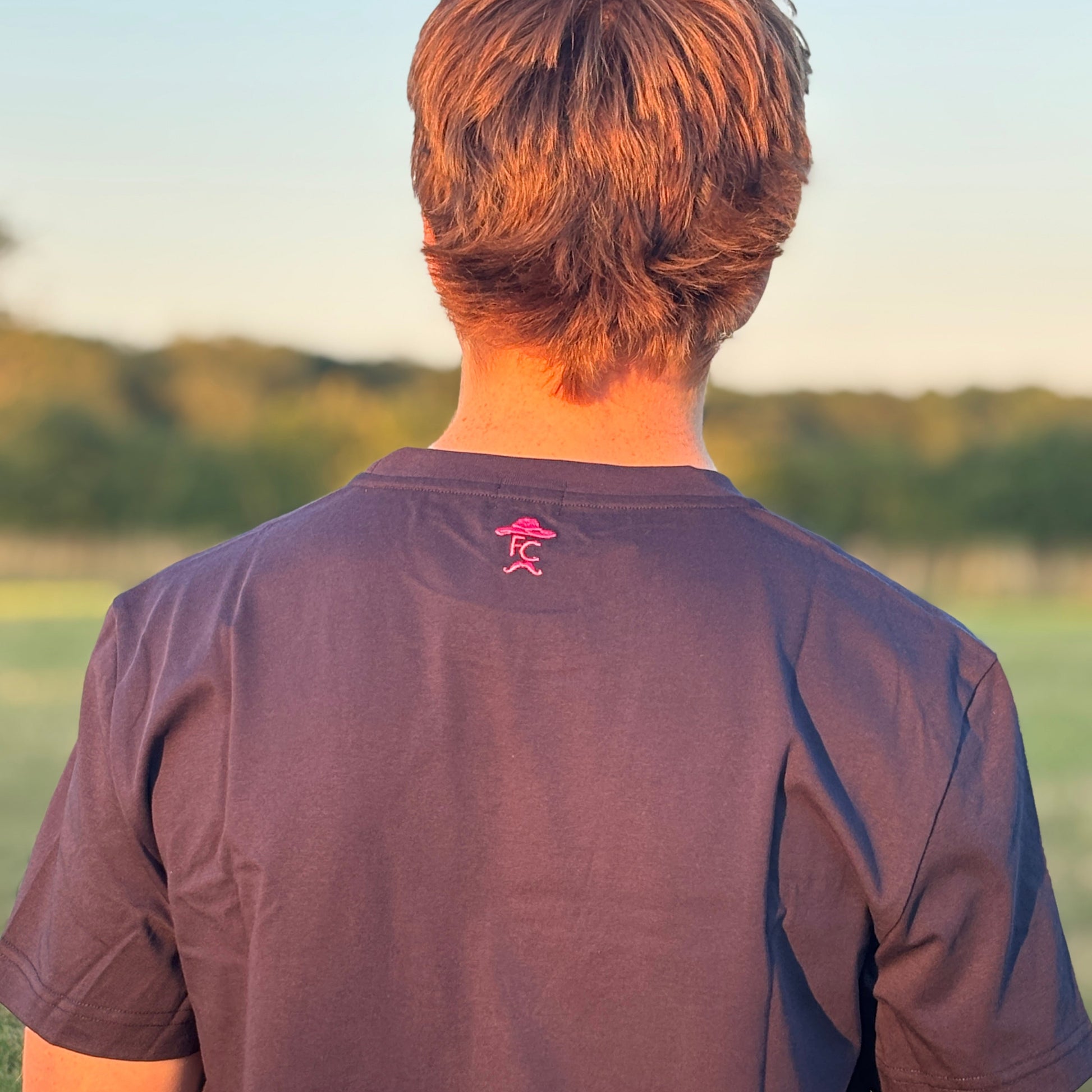 Person wearing a dark blue t-shirt with a logo on the back, standing outdoors with a scenic background.