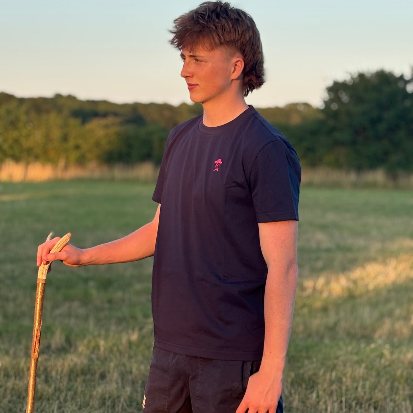 Person holding a walking stick in a field with trees in the background
