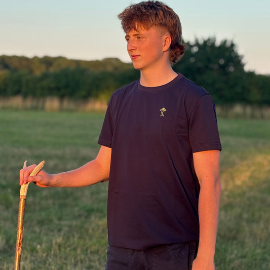 Person wearing a Fen Cowboys dark blue t-shirt with a logo, standing in a field holding a walking stick.