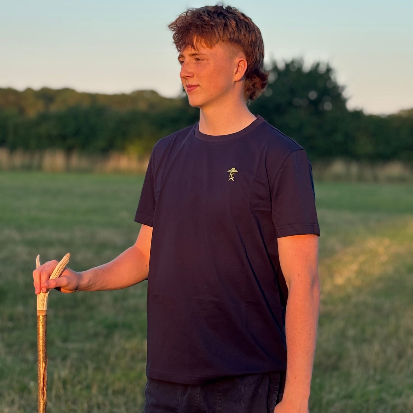 Person holding a cane in a field with trees in the background