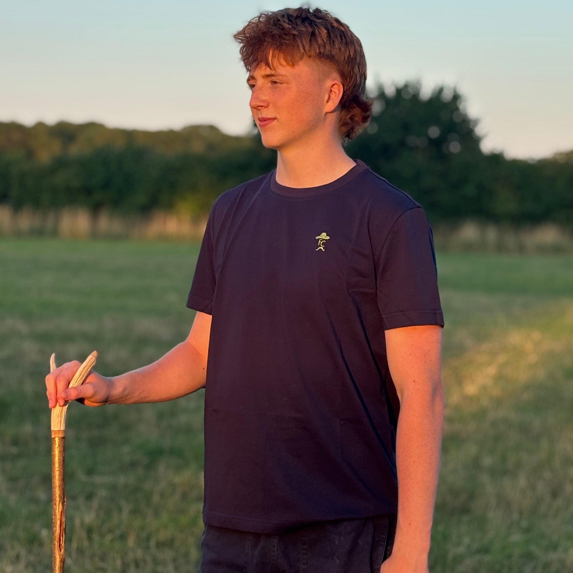Person holding a cane in a field with trees in the background