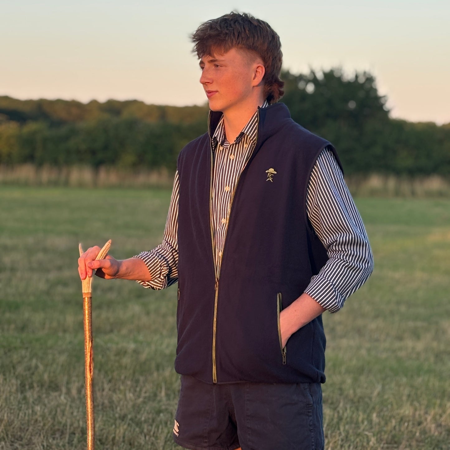 Person wearing a Fen Cpwboys gilet and holding a walking stick in a field