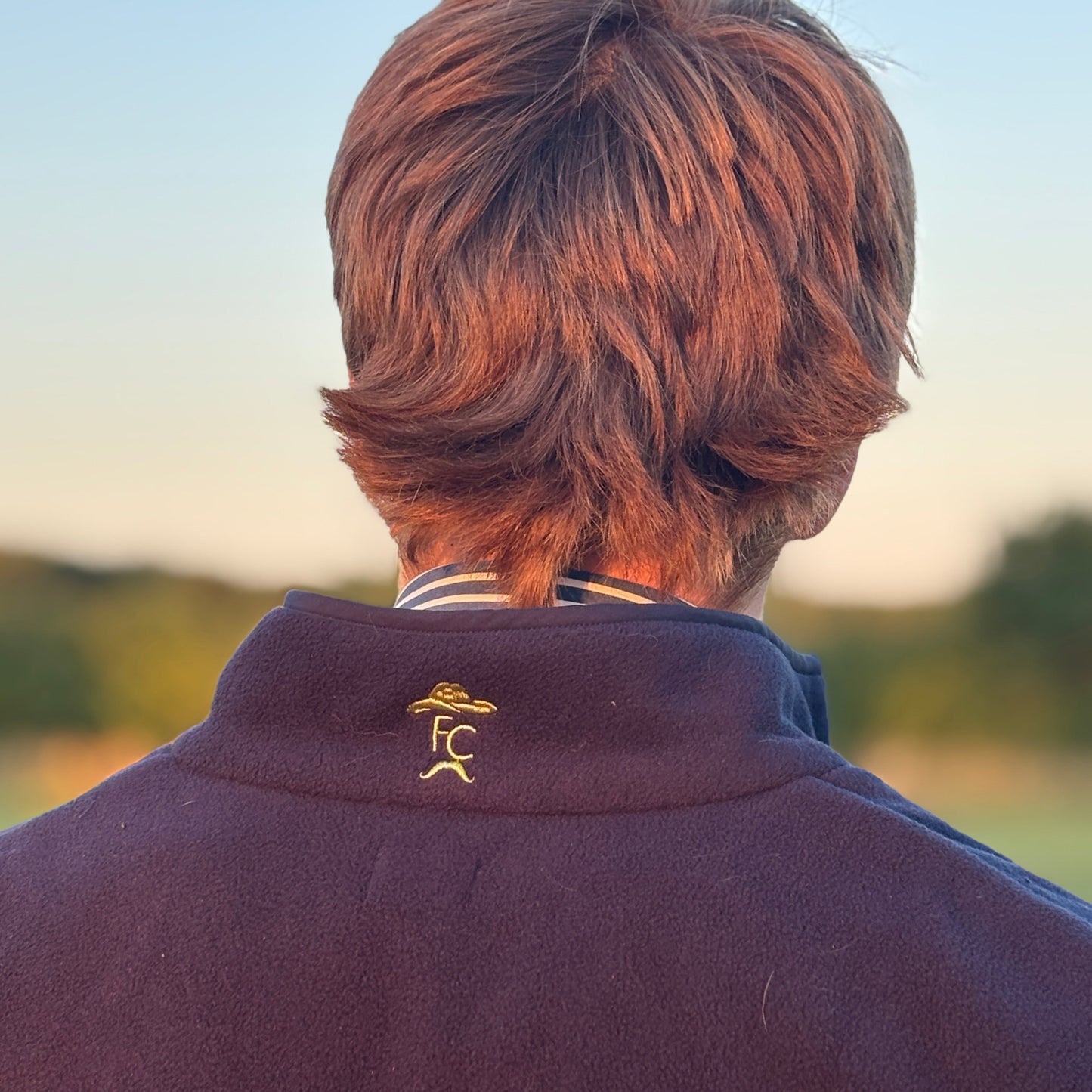 Person wearing a jacket with a logo, standing outdoors with a blurred background
