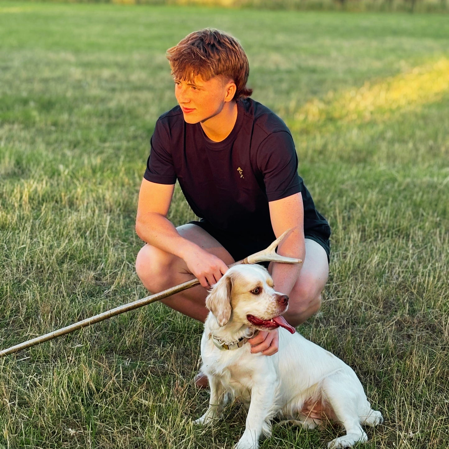 Person sitting with a Clumber Spaniel in a grassy field