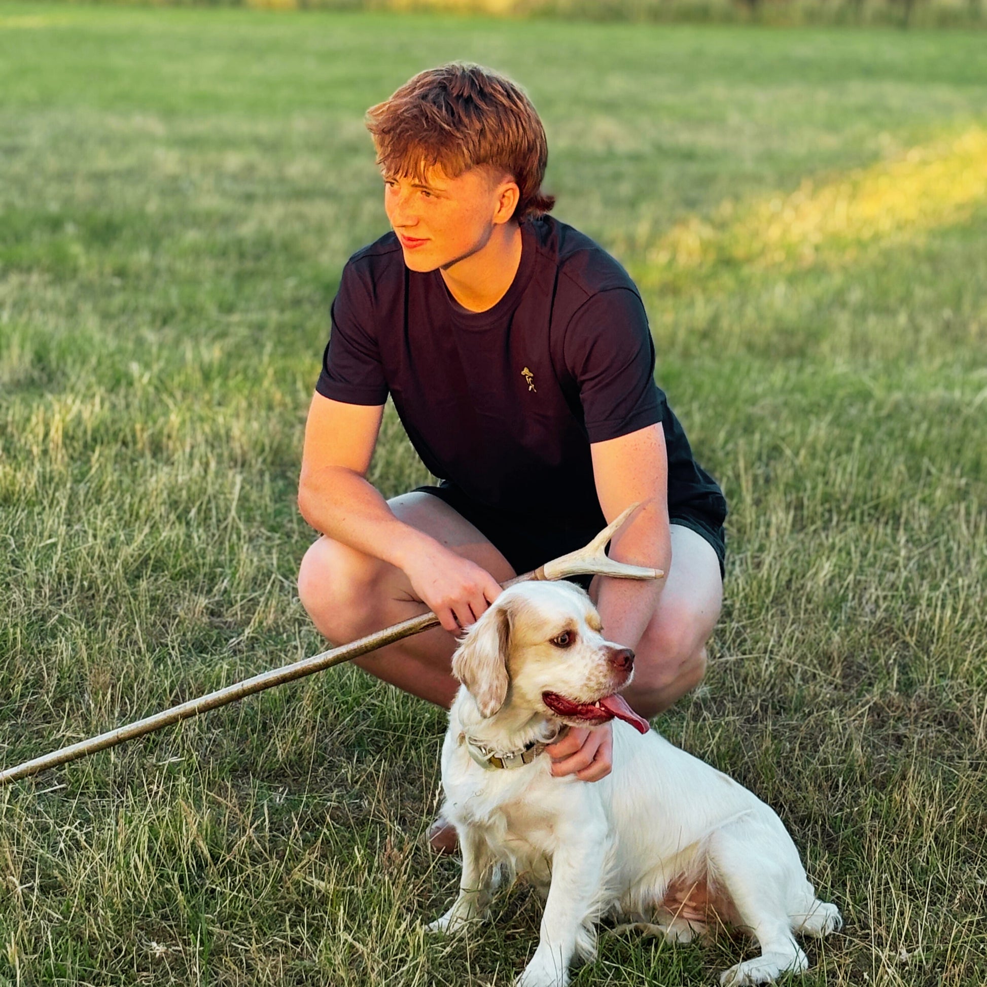 Person sitting with a Clumber Spaniel in a grassy field